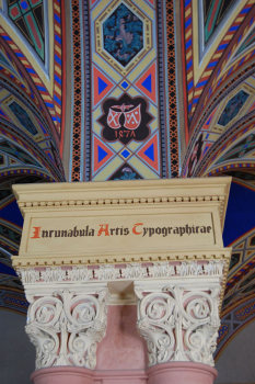The coats of arms of the pioneer printers, painted above the column capitals of the middle pillar